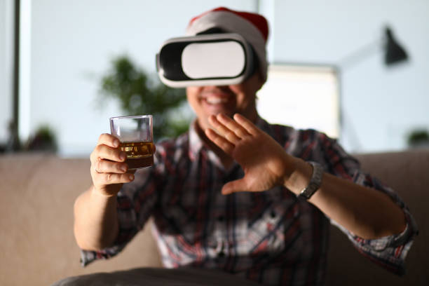 l'homme s'asseyent au verre de prise de sofa dans la main et utilisant des gogles de vr - gogles photos et images de collection