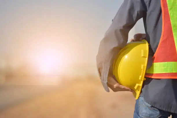Photo of Close up Engineering holding Yellow helmet hard hat safety and Road construction background
