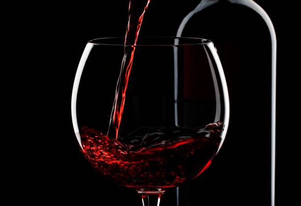 istock Pouring red wine into the glass against red black background 1197406229