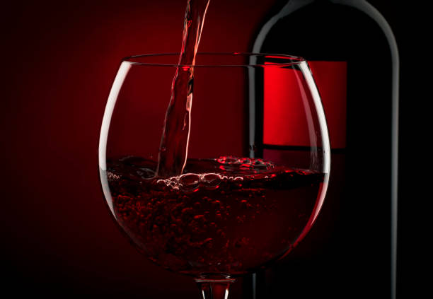 istock Pouring red wine into the glass against red black background 1197406241
