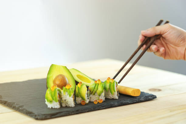 japanese avocado sushi on black slate stone and wood table with hand on shop-stick for eating