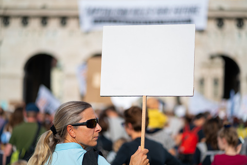 forty years old woman holding white sign with place for text at climate change demonstration with many blurred people in european city of vienna austria
