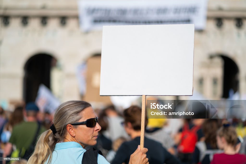 climate activist with white sign at fridays for future demonstration forty years old woman holding white sign with place for text at climate change demonstration with many blurred people in european city of vienna austria Protest Stock Photo