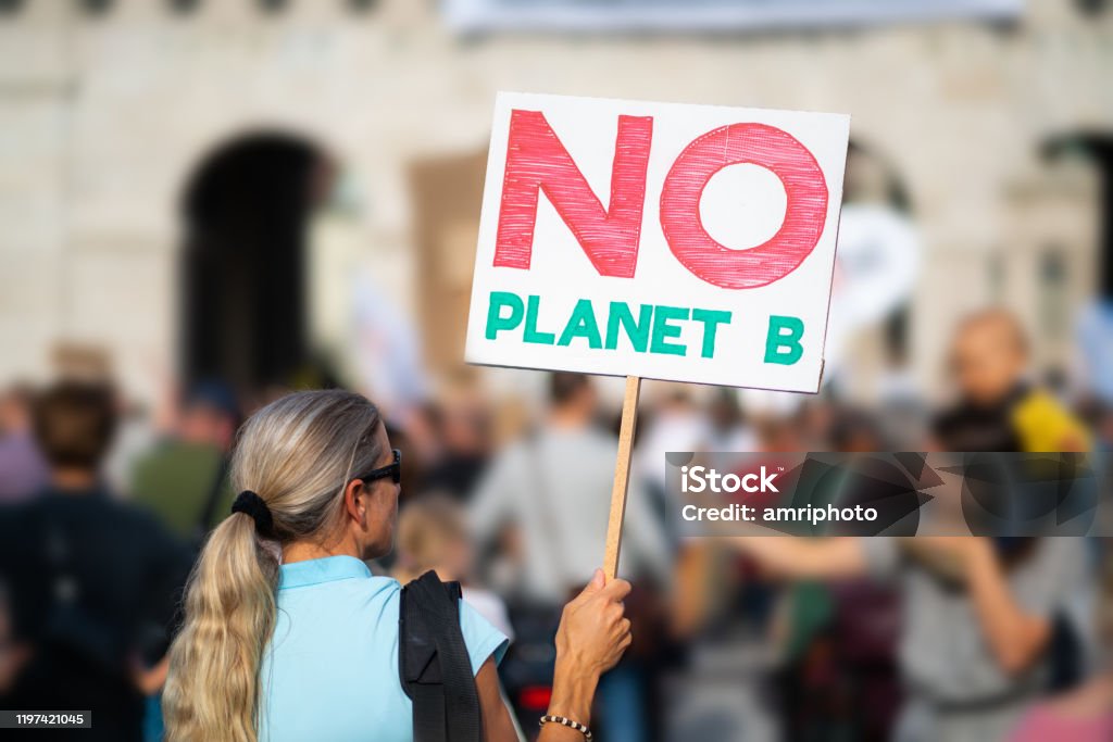 rear view woman with sign at climate change demonstration woman holding no planet b sign at protest march demonstration against climate change in european city, shallow focus, background blurred Protest Stock Photo