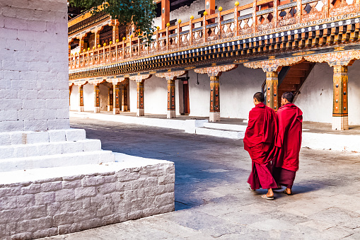 Punakha/ Bhutan - February 28, 2016: two Buddhist monks in their traditional red dress walking in the monastery Punakha Dzong courtyard, Bhutan.