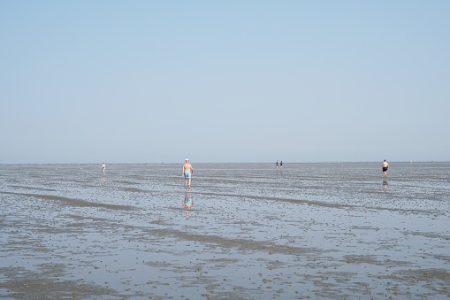 Cuxhaven, Germany - August 26, 2019: North sea coast at ebb tide. Incidental people walking across mudflat tideland.