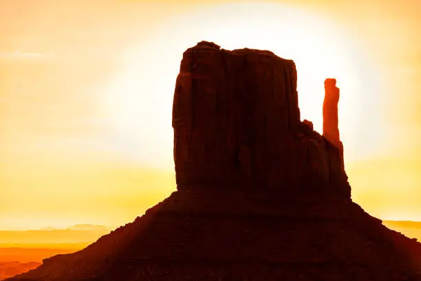 View closeup of one famous mesa butte mitten formations with red orange rock color on horizon in Monument Valley canyons during sunrise in Arizona