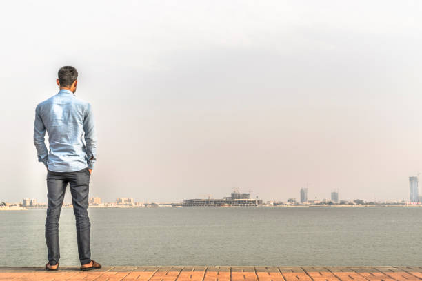 Man in a vibrant red hoodie stands gazing out at a dramatic coastal landscape.