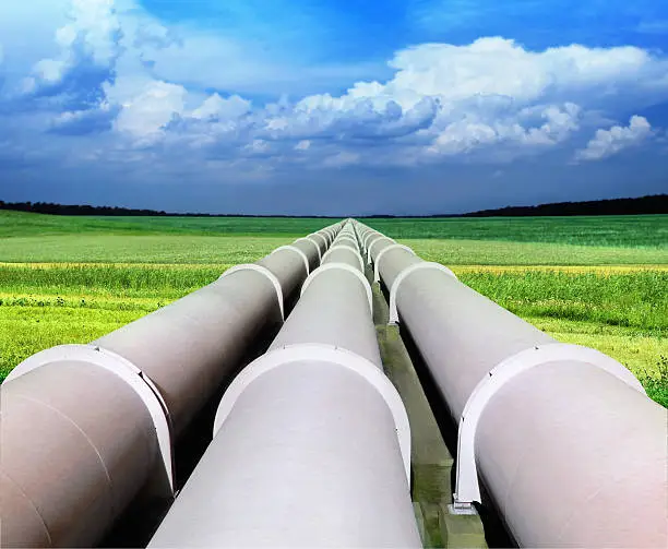 Photo of Three gas pipelines in a green field with blue sky