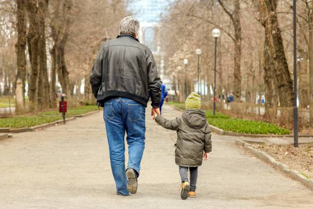 Little caucasian boy walks with old-aged man, holding him with hand. Little caucasian boy walks with old-aged man, holding him with hand. Stroll in autumn park, casual wear, mood atmosphere, grandson with grandfather. Outdoors, copy space. kidnapping photos stock pictures, royalty-free photos & images