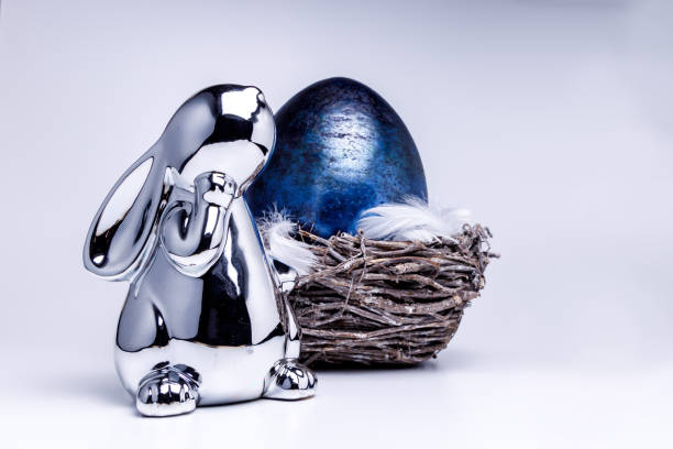 figure de lapin de pâques dans l'argent et un oeuf bleu de pâques dans un panier de pâques avec des plumes - figurine easter egg easter holiday photos et images de collection