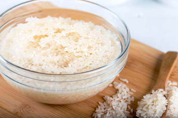 Soaked rice, grain, cloudy liquid water in glass bowl on wooden background Soaked rice, grain, cloudy liquid water in glass bowl on wooden background drenched stock pictures, royalty-free photos & images