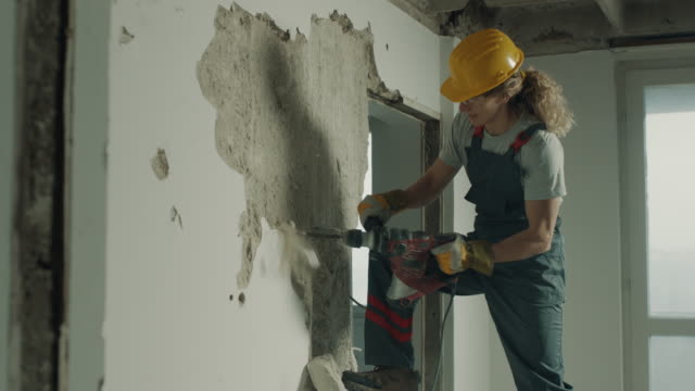 Construction worker demolishing the wall with electric drill