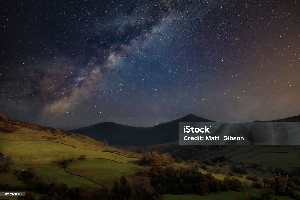 Beautiful Autumn Fall landscape view of mountains in beautiful golden sunlight against dramatic sky Beautiful epic digital composite landscape of Milky Way over Keswick in Lake District Night Stock Photo