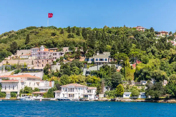 Beautiful builings and mansions at the costline and hillslope with Turkish national flag and green forest in summer, at Bosphorus Strait in Istanbul,Turkey. View from a Cruise Ship.