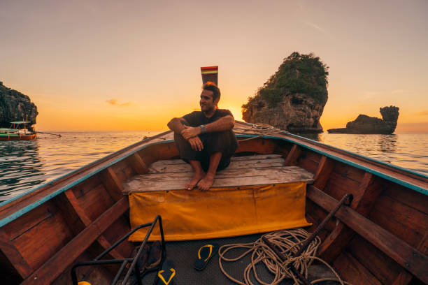 Young man on a longtail boat in Thailand during sunset, Phi Phi Island