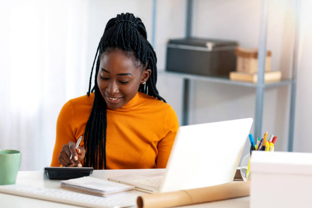 Making money work for her business Close up of one African American woman using calculator, calculating finance at home, female hands and paper document at table close up, economist or financier writing report, student doing homework refund stock pictures, royalty-free photos & images