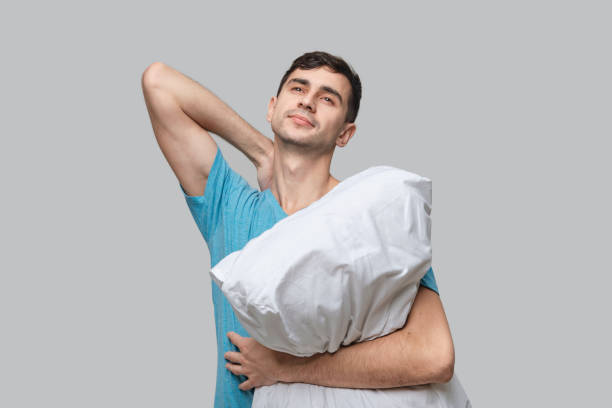 istock Young brunet man dreaming holding white pillow isolated over grey background. 1197485029