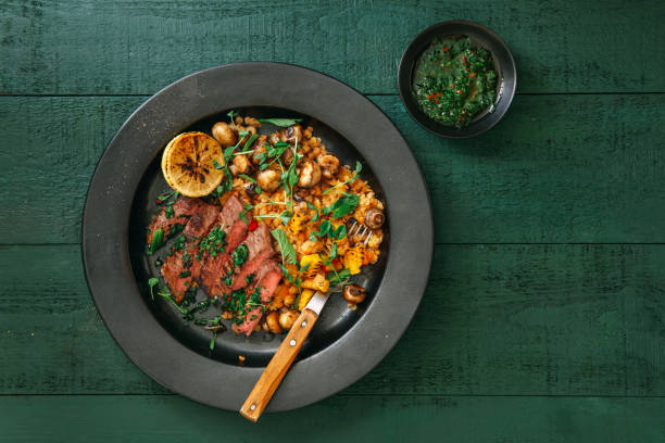 Steak with lentil salad Steak with herb sauce, grilled vegetables, pea and lentil salad on green background. Top view. chimichurri stock pictures, royalty-free photos & images