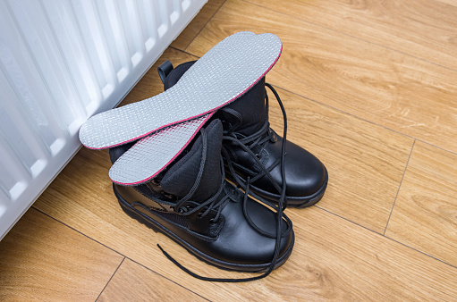 Plantillas de papel de aluminio caliente para calzado de invierno como patas de protección contra el frío y helado. Las botas de invierno se están secando cerca del radiador de calefacción. Enfoque selectivo, primer plano. photo