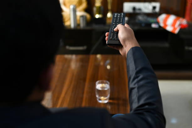 Man drinking soda juice and looking at TV with legs on the table in living room.