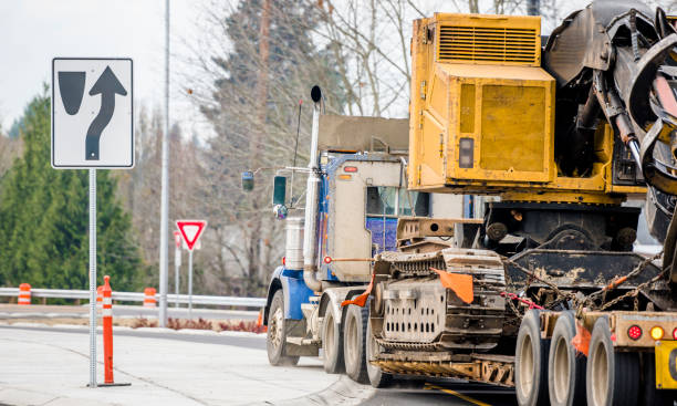 istock Big rig powerful blue classic semi truck transporting oversize load equipment on the step down semi trailer driving on the round road intersection 1197507693