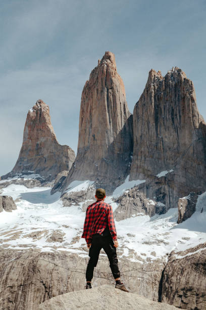 A man stands on a rock and looks at Mirador Base Las Torres in Torres del Paine National Park A man in a red checkered shirt stands on a rock and looks at Mirador Base Las Torres in Torres del Paine National Park mirador stock pictures, royalty-free photos & images
