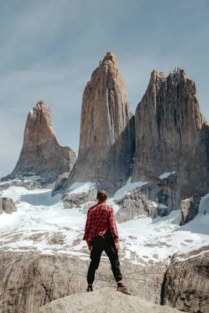 A man in a red checkered shirt stands on a rock and looks at Mirador Base Las Torres in Torres del Paine National Park
