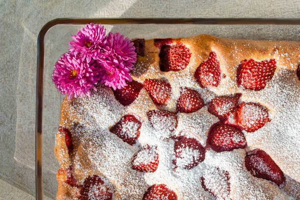 Cake with strawberries sprinkled with powdered sugar in a glass form with chrysanthemums