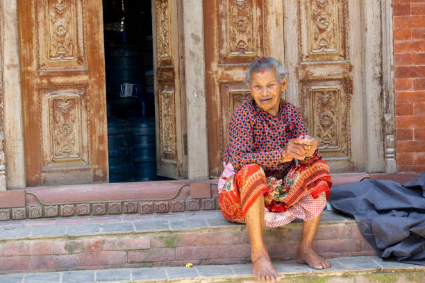 kathmandu, nepal, 20 giugno 2019: tempio di changu narayan, sulla strada per raggiungere il tempio incontro un'anziana seduta di fronte a un'antica porta di legno scolpita con figure mitologiche - changu narayan temple foto e immagini stock