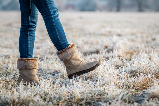 Walking outdoors in hoarfrost. Female legs with skinny jeans walks in frozen grass