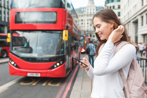 Happy woman with smartphone at bus stop in London Happy woman with smartphone at bus stop in London - Smiling girl looking at her phone and checking bus timetable on a day out in London - Lifestyle and transportation concepts inner london stock pictures, royalty-free photos & images