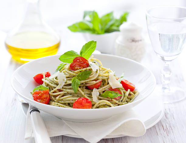 Plated spaghetti with pesto, tomatoes, and shaved Parmesan