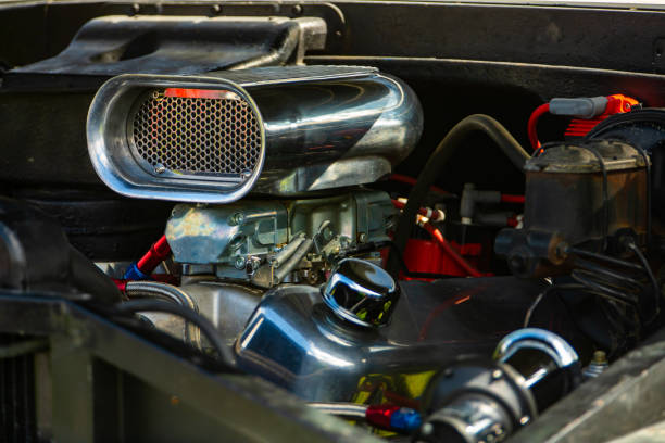 A detailed close-up view of a car engine compartment with the hood open, captured during a roadside breakdown on a sunny day. The image shows various automotive components including the car battery, radiator, hoses, and engine parts, emphasizing real-life vehicle maintenance, mechanical issues, and car troubleshooting scenarios. Ideal for illustrating concepts such as car repair, emergency assistance, travel problems, and automotive safety