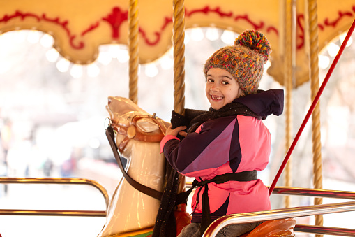 A little girl rides on a carousel, winter holidays.