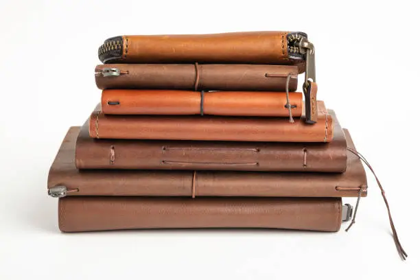 A stack of leather-bound journals, notebooks, cases and wallets set on a plain white background.