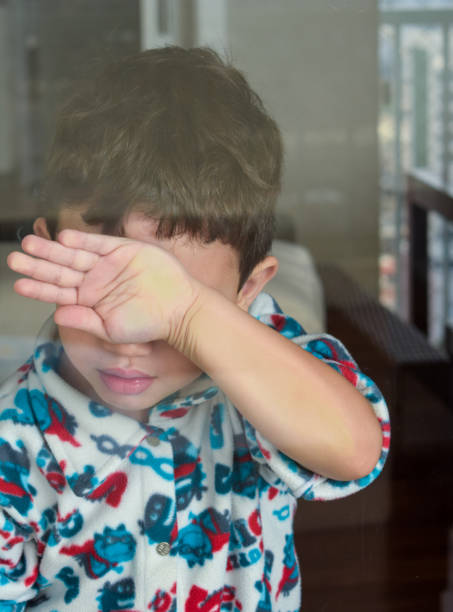 istock Child hiding face with hand behind glass. 1197547081