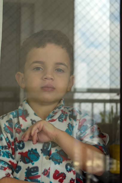 istock 5 year old boy looking serious behind glass. 1197547082