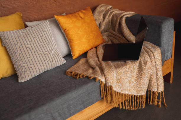 Laptop on gray sofa with yellow pillows.