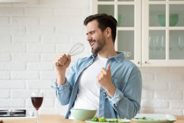 Funny guy singing holding beater microphone cooking in modern kitchen