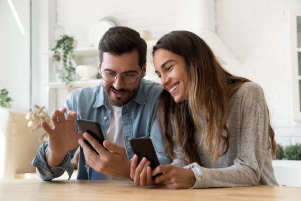 スマートフォンを使用して若いカップルは、自宅でソーシャルメディアのニュースを共有します - two girls ストックフォトと画像