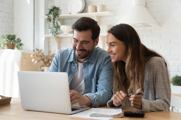 Happy young couple paying bills online in computer app Happy young couple husband and wife using laptop computer looking at screen pay bills online in app calculate mortgage investment payment on website planning budget discuss finances sit at home table home finances stock pictures, royalty-free photos & images