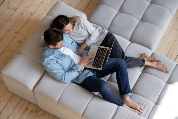 istock Happy young couple using laptop relaxing on sofa, top view 1197547536