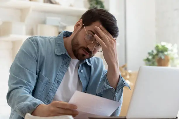 Photo of Upset frustrated young man holding reading postal mail letter