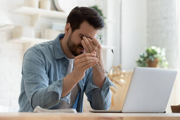 Tired young man feel eyestrain holding glasses fatigued from computer