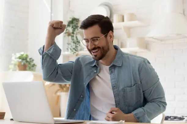 Photo of Excited young man looking at laptop celebrating online victory