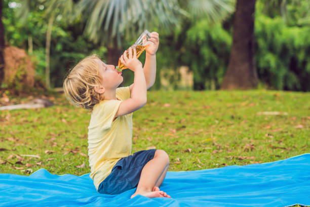 A boy drinks lemonade, tea, kombucha, an orange drink in the park.