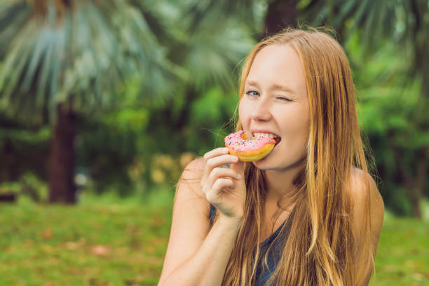 portrait of a young woman eating a donut against a plant background portrait of a young woman eating a donut against a plant background. big fat lips stock pictures, royalty-free photos & images