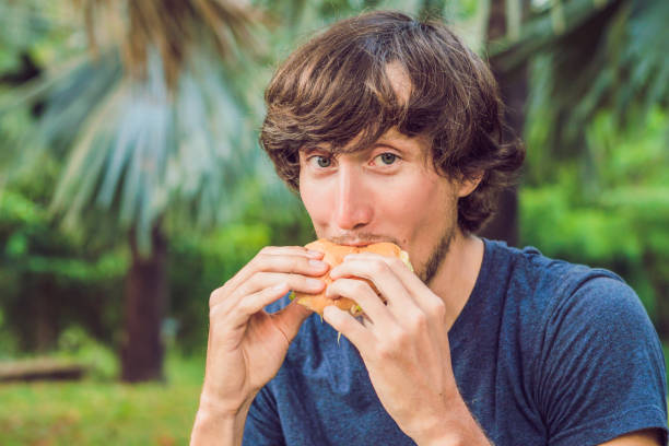 istock Young man eating a hamburger in the park 1197557736