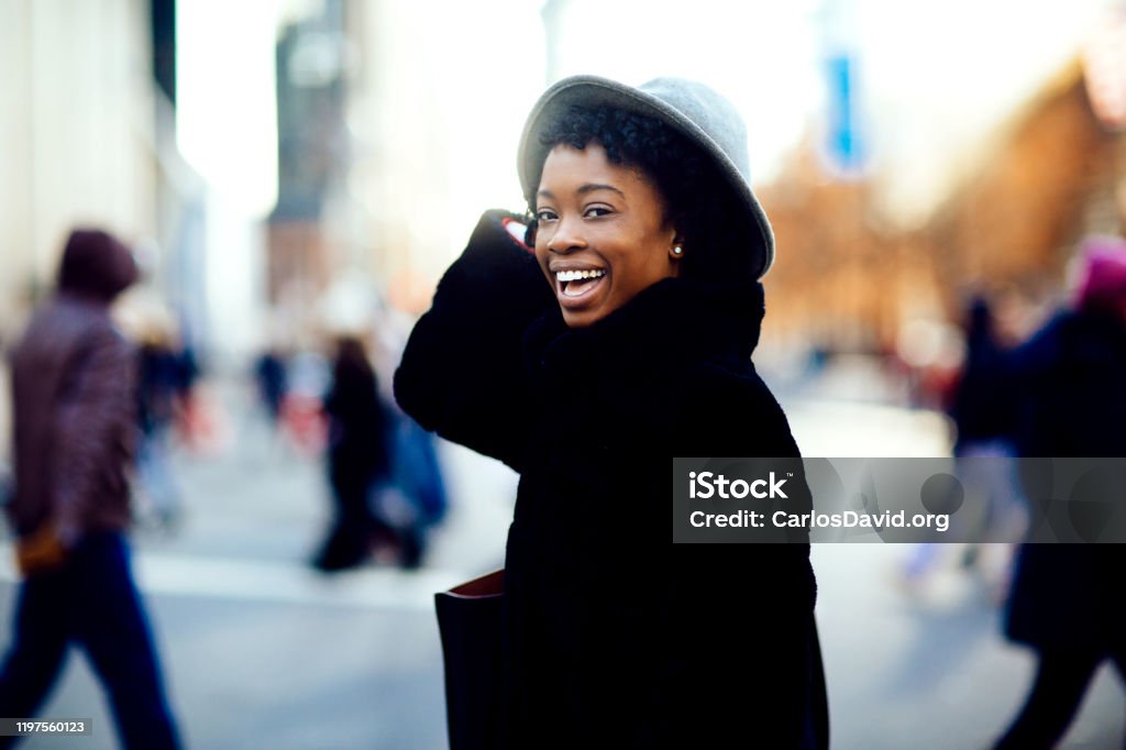 Portrait of a happy smiling woman in faux fur coat and hat laughing at camera while crossing a busy urban street Crossing Stock Photo